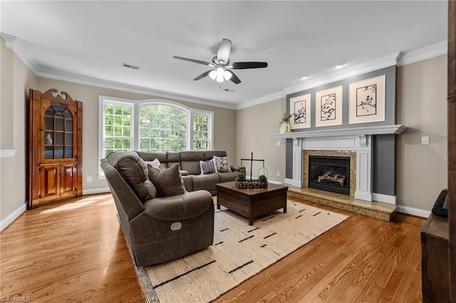 living room with ceiling fan, light wood-style floors, a high end fireplace, visible vents, and ornamental molding