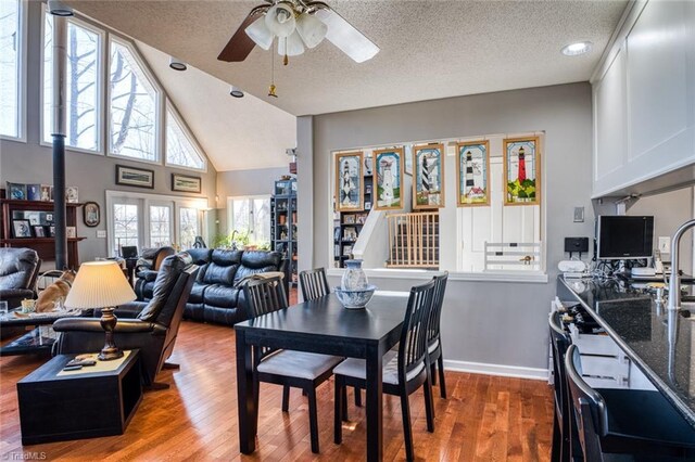 dining area featuring wood finished floors, a ceiling fan, baseboards, high vaulted ceiling, and a textured ceiling