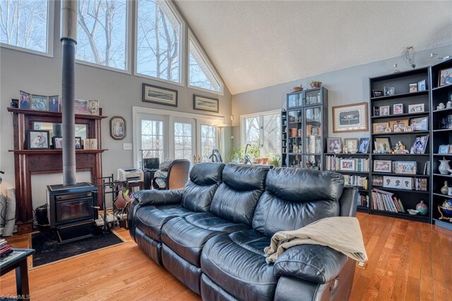 living area featuring high vaulted ceiling, a textured ceiling, a wood stove, and wood finished floors