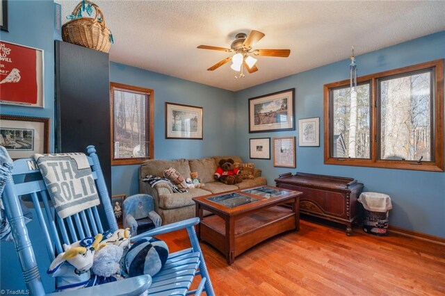 living area with a textured ceiling, baseboards, light wood-type flooring, and ceiling fan
