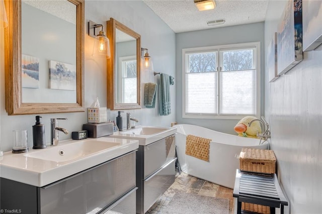 bathroom with a sink, a freestanding tub, two vanities, and a textured ceiling
