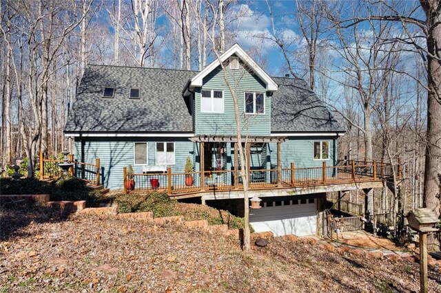 rear view of house featuring a deck, an attached garage, and a shingled roof