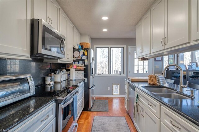 kitchen featuring light wood-style flooring, a sink, appliances with stainless steel finishes, white cabinetry, and tasteful backsplash