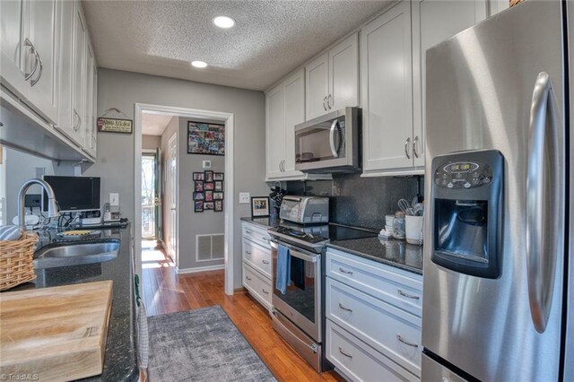 kitchen featuring visible vents, light wood-style flooring, a sink, stainless steel appliances, and a textured ceiling
