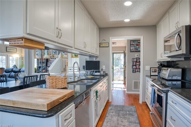 kitchen featuring visible vents, light wood-style floors, white cabinets, stainless steel appliances, and a sink