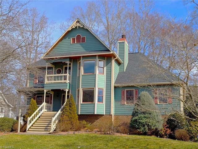 victorian home featuring a balcony, brick siding, stairway, a front lawn, and a chimney