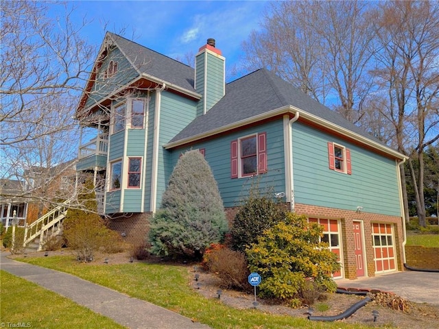 view of side of home featuring driveway, a garage, a balcony, a chimney, and brick siding