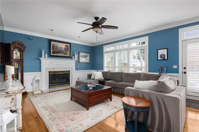 living room featuring a fireplace, light hardwood / wood-style flooring, ornamental molding, and ceiling fan