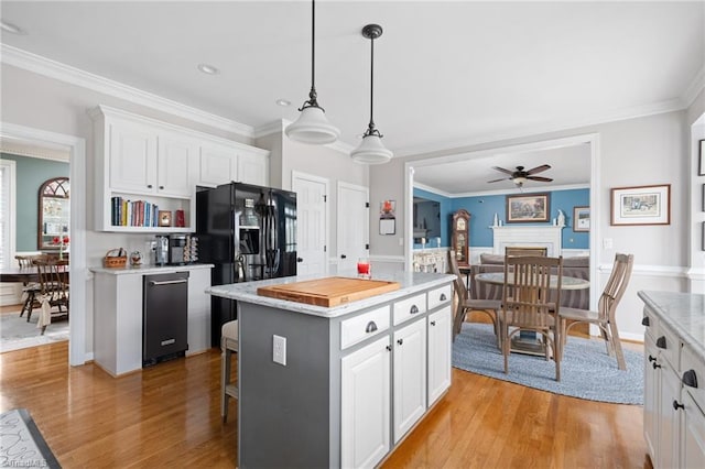 kitchen with white cabinetry, hanging light fixtures, black fridge, and a kitchen island