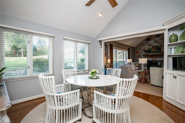 dining space featuring dark hardwood / wood-style flooring, a stone fireplace, and vaulted ceiling