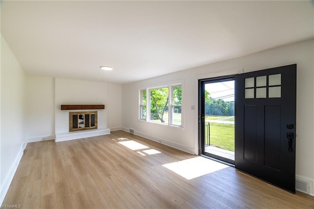 unfurnished living room with light wood finished floors, baseboards, and a brick fireplace