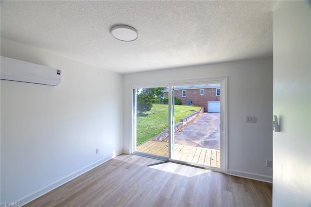 spare room featuring wood finished floors, a wall unit AC, baseboards, and a textured ceiling