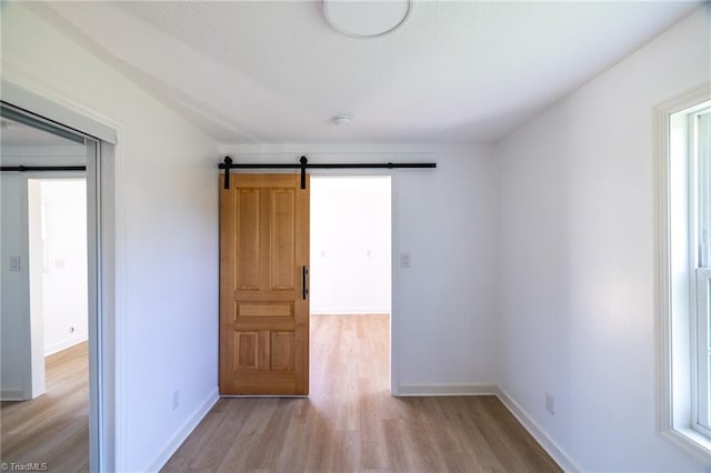 empty room featuring a barn door, light wood-style flooring, baseboards, and plenty of natural light