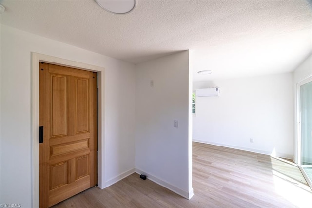spare room with wood finished floors, a wall unit AC, a textured ceiling, and baseboards