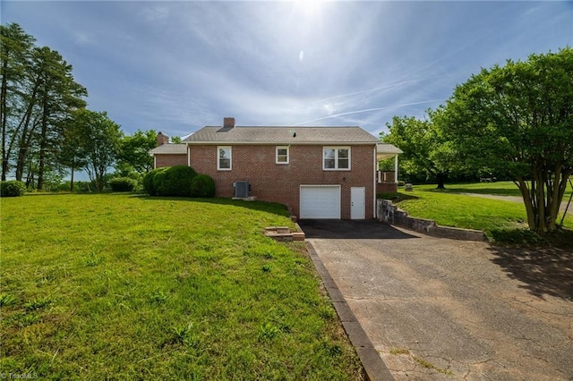 view of side of home featuring driveway, brick siding, a garage, a chimney, and a yard