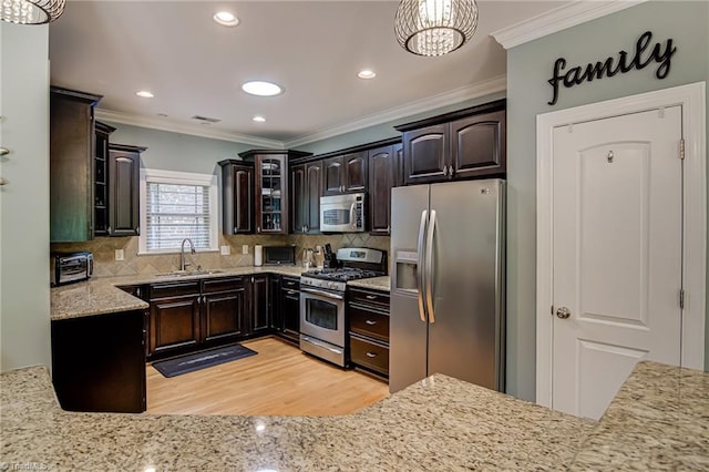 kitchen with stainless steel appliances, a sink, crown molding, glass insert cabinets, and light wood-type flooring
