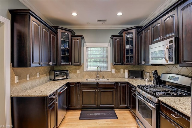 kitchen with appliances with stainless steel finishes, a sink, dark brown cabinets, light stone counters, and ornamental molding