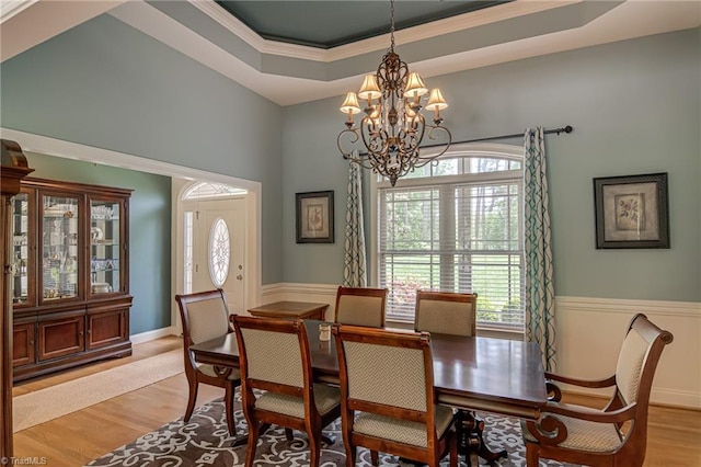 dining area featuring a chandelier, healthy amount of natural light, a raised ceiling, a wainscoted wall, and light wood-style floors