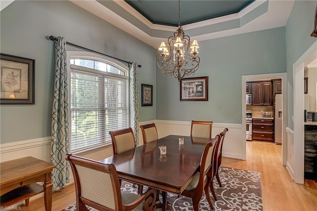 dining area with light wood-style flooring, a chandelier, and a tray ceiling