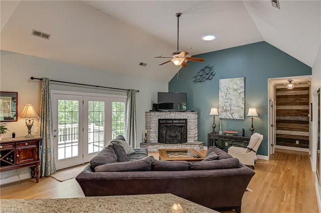 living area featuring ceiling fan, light wood-style flooring, a fireplace, high vaulted ceiling, and baseboards