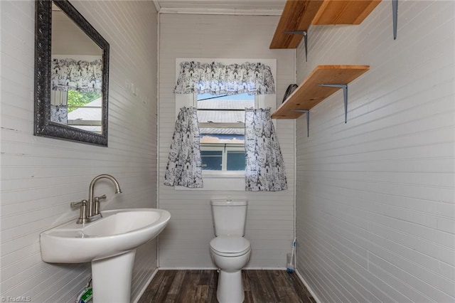 half bath with toilet, wood finished floors, a sink, and tile walls