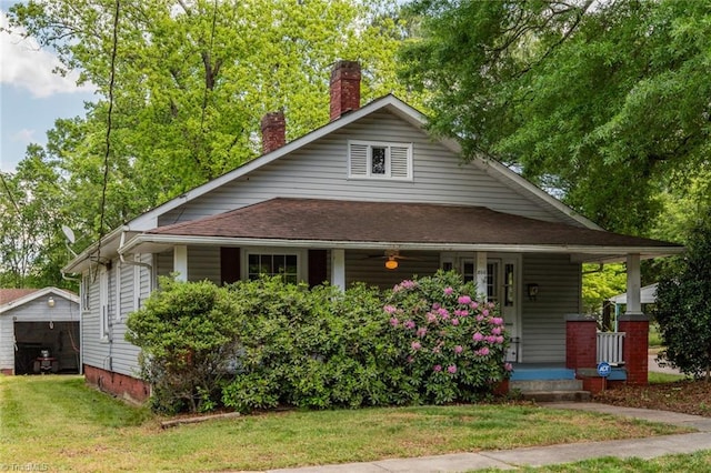view of front of home with a porch, a front lawn, a chimney, a detached garage, and an outdoor structure