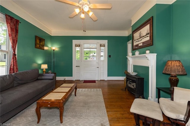 living area featuring ceiling fan, a wood stove, wood finished floors, crown molding, and baseboards