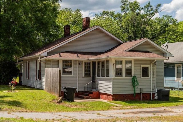 view of front of home featuring entry steps, a chimney, cooling unit, a front yard, and roof with shingles