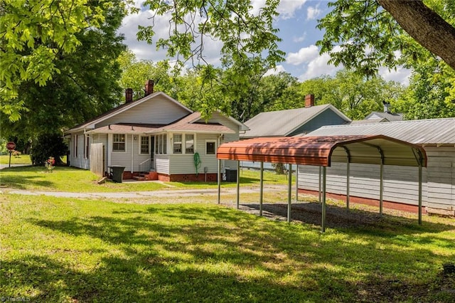 back of property featuring a detached carport, entry steps, dirt driveway, and a yard
