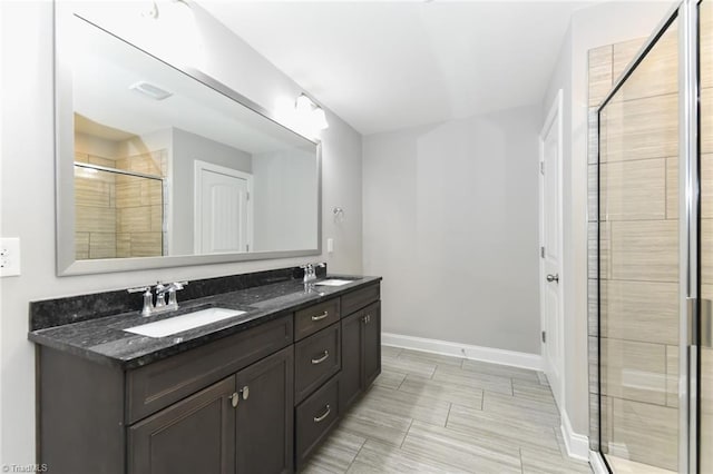 full bathroom with double vanity, baseboards, a shower stall, and a sink