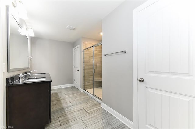 full bathroom featuring double vanity, wood tiled floor, a stall shower, a sink, and baseboards