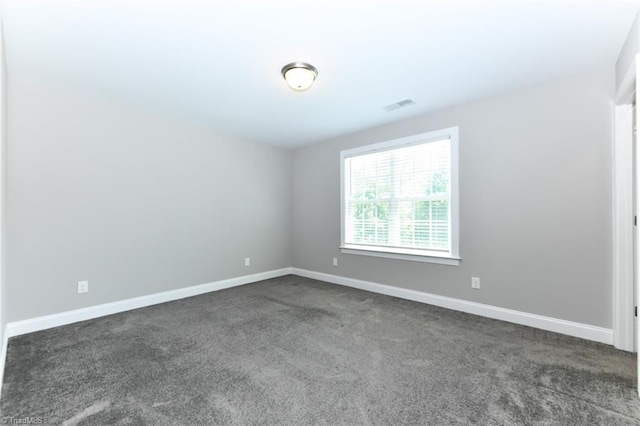 unfurnished room with baseboards, dark carpet, and visible vents