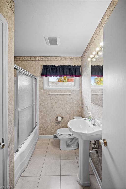 bathroom featuring tile patterned flooring, bath / shower combo with glass door, and toilet