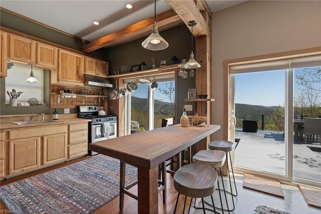 kitchen featuring light brown cabinetry, under cabinet range hood, a sink, beam ceiling, and gas stove