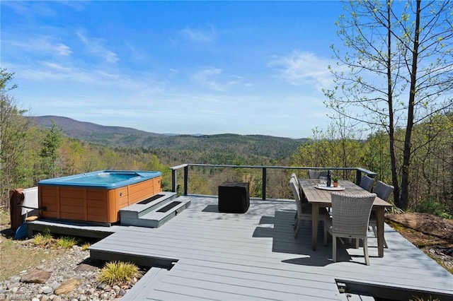 wooden terrace featuring a mountain view, a view of trees, a hot tub, and outdoor dining space