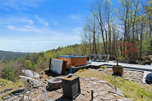 view of yard with a view of trees, a hot tub, an outdoor fire pit, and a deck