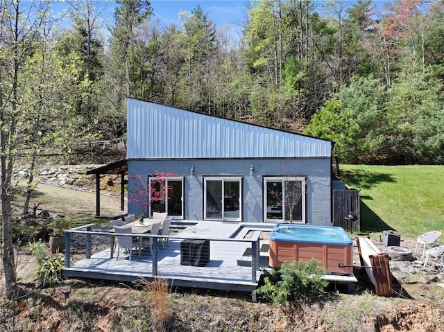 back of house featuring a wooded view, a wooden deck, a hot tub, a yard, and an outdoor fire pit