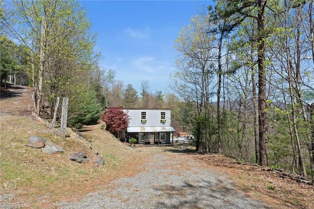 view of front facade with dirt driveway and a forest view