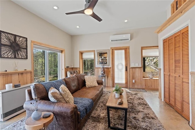 living area with a wall mounted air conditioner, a ceiling fan, a wainscoted wall, wood walls, and recessed lighting