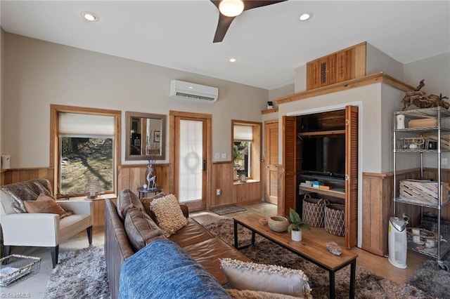 living area with wainscoting, ceiling fan, a healthy amount of sunlight, and a wall unit AC