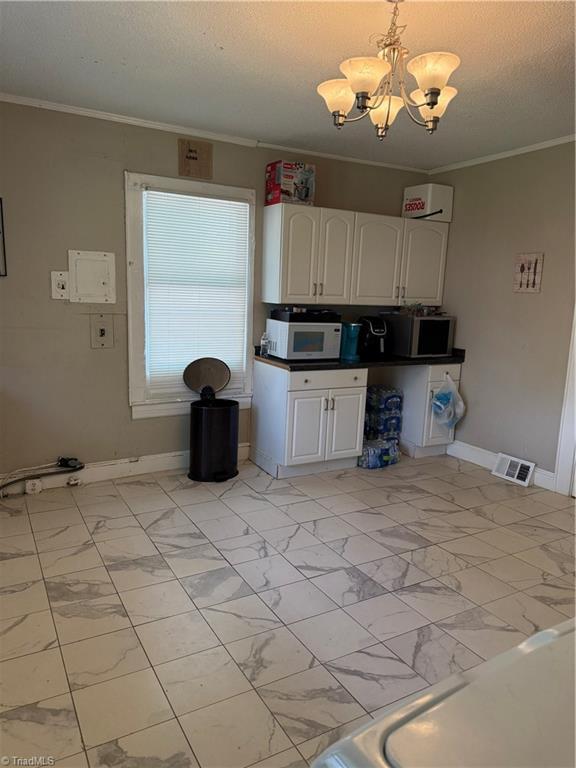 kitchen with white cabinets, marble finish floor, baseboards, white microwave, and a notable chandelier