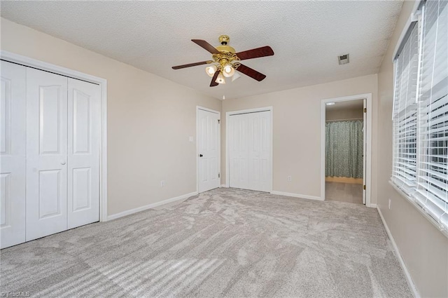 unfurnished bedroom featuring light carpet, visible vents, a textured ceiling, and two closets