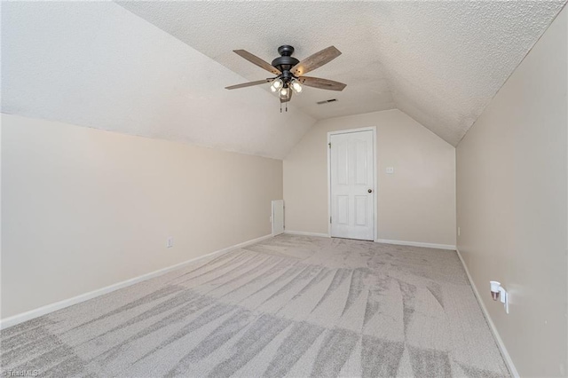 bonus room with a textured ceiling, lofted ceiling, light carpet, visible vents, and baseboards