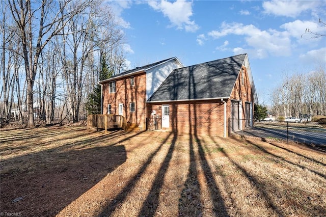 view of home's exterior with brick siding, a shingled roof, fence, dirt driveway, and a lawn