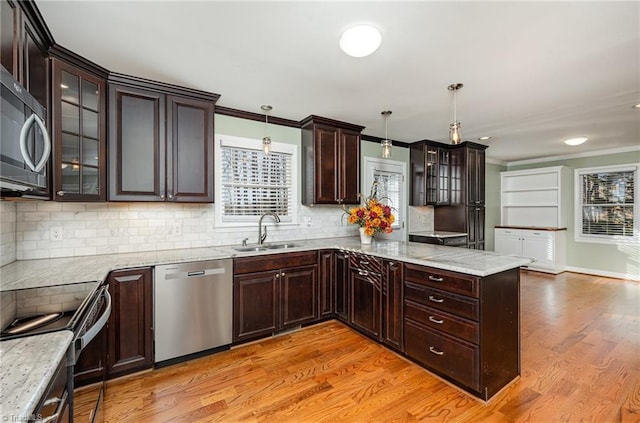 kitchen with glass insert cabinets, ornamental molding, stainless steel appliances, pendant lighting, and a sink