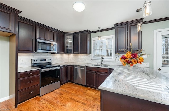 kitchen with dark brown cabinetry, light wood-style flooring, appliances with stainless steel finishes, pendant lighting, and a sink