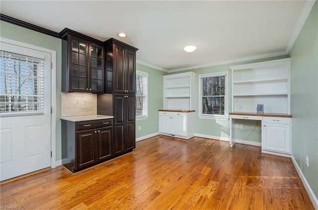 kitchen featuring glass insert cabinets, light wood-style floors, ornamental molding, built in study area, and dark brown cabinets