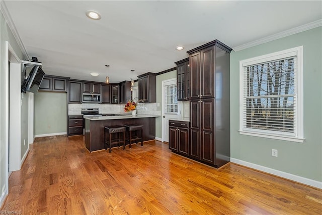 kitchen with crown molding, a breakfast bar area, stainless steel appliances, light countertops, and dark brown cabinetry