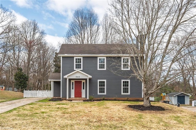 view of front facade featuring a front yard, fence, a chimney, and an outbuilding