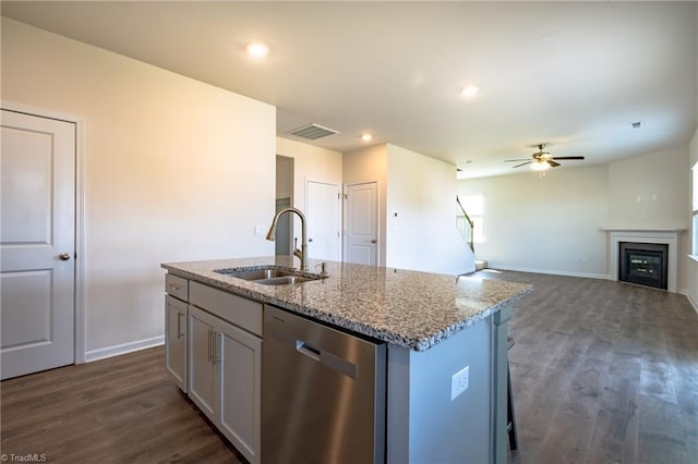 kitchen with dishwasher, a sink, ceiling fan, dark wood finished floors, and light stone countertops